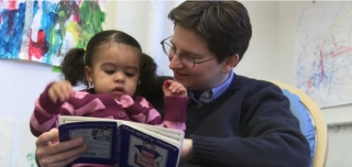 A little girl sitting on her teacher’s lap while she reads her a book at The Whole Child Development Center